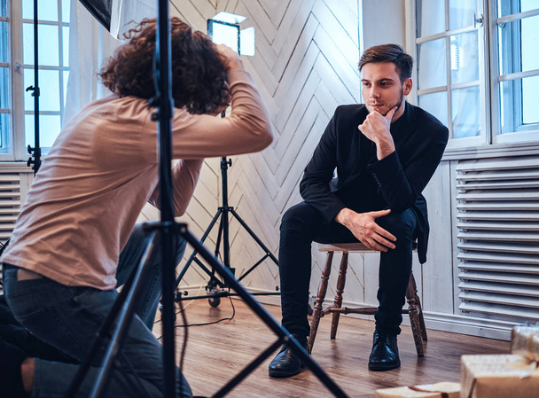  Fotoshooting im Studio: Ein gutaussehender junger Kerl sitzt, lächelt und posiert - Foto, Bild