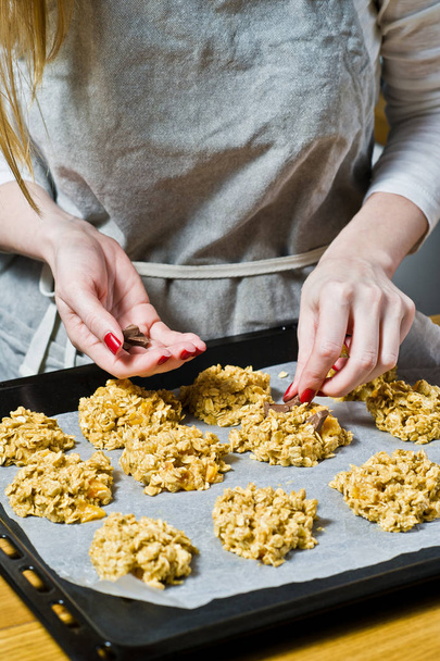 Female chef preparing oatmeal cookies, spread the dough on the trays. Side view, black background, kitchen. - Photo, Image