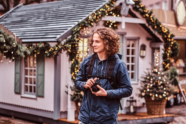 A young handsome curly traveler smiles, walks through the holiday city - Photo, Image