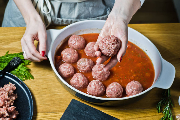 O chef prepara almôndegas suecas da carne picada crua, instala em uma assadeira com molho de tomate. Fundo preto, vista superior, cozinha
 - Foto, Imagem