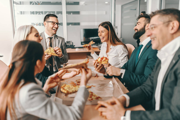 フォーマルウェアの幸せな同僚の小さなグループは、昼食のために一緒におしゃべりやピザを食べます。一人で私たちはほとんど何もできない、一緒に私たちはそんなに多くを行うことができます. - 写真・画像