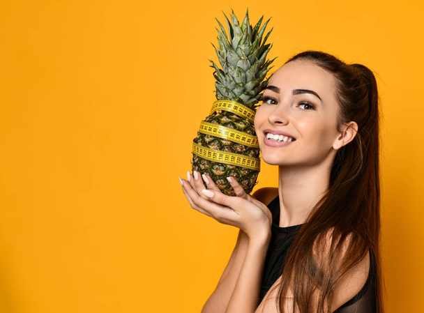 Sporty woman waist with measure tape and pineapple isolated on yellow background. - Photo, Image