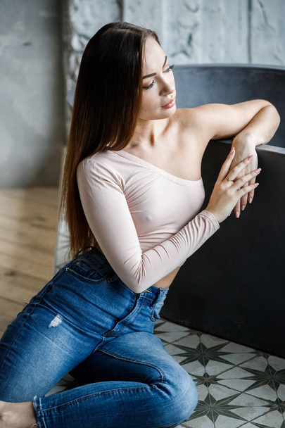 Portrait of beautiful young woman in blue jeans and beige t-shirt. Young model sitting on floor at luxury apartments interior - Foto, immagini