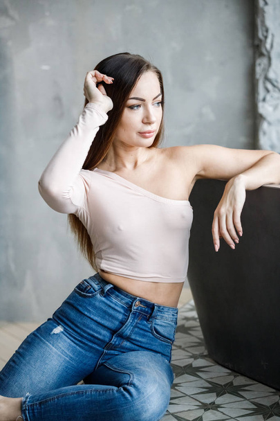 Portrait of beautiful young woman in blue jeans and beige t-shirt. Young model sitting on floor at luxury apartments interior - Foto, Imagen