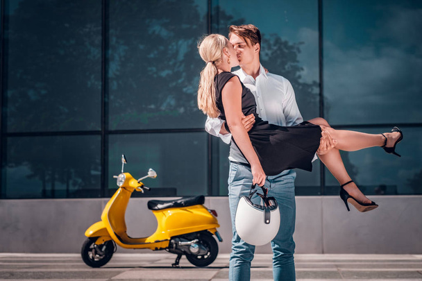 Ρομαντικό ζευγάρι στην αγάπη, ένας τύπος φιλιά την κοπέλα που κρατά στα χέρια του, ενώ στέκεται σε ένα ουρανοξύστη στο κέντρο της πόλης - Φωτογραφία, εικόνα