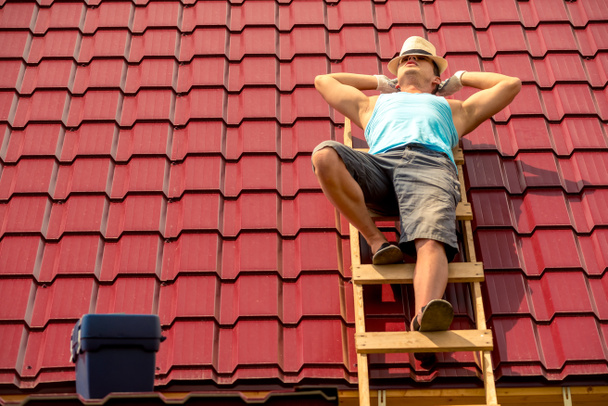 trabajador descansando en el sol en las escaleras en el techo de la casa, sobre el fondo de azulejos - Foto, Imagen