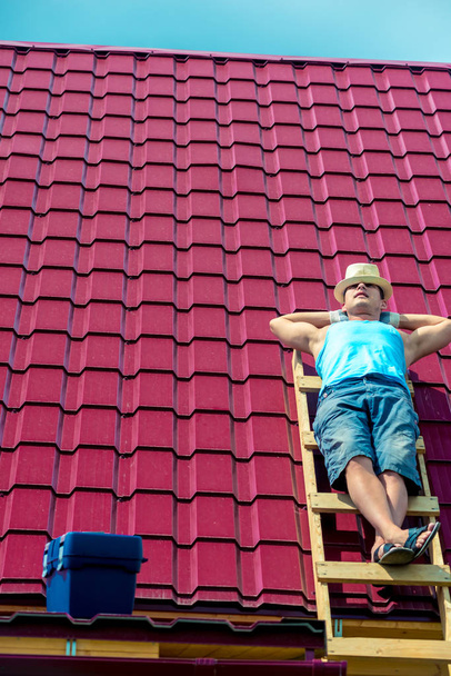 Ένας εργάτης κάνει ηλιοθεραπεία στην οροφή του σπιτιού κατά τη διάρκεια ενός διαλείμματος. - Φωτογραφία, εικόνα