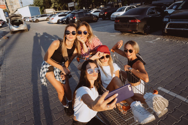 Cinco jovens se divertem com um carrinho de supermercado em um parque de estacionamento
 - Foto, Imagem