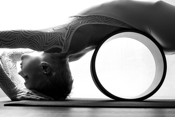 Portrait of gorgeous young woman practicing yoga indoor with a help of yoga wheel - Фото, зображення