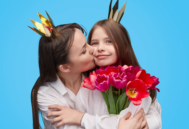 Loving woman kissing girl with holiday flowers in hands  - Photo, Image