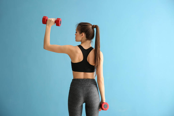 Urheilullinen nuori nainen käsipainoilla värillisellä taustalla - Valokuva, kuva
