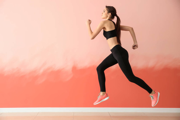 Sporty young woman running against color wall - Photo, Image