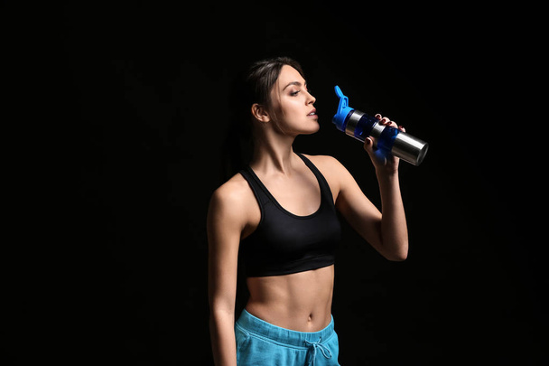 Desportivo jovem mulher beber água no fundo escuro
 - Foto, Imagem