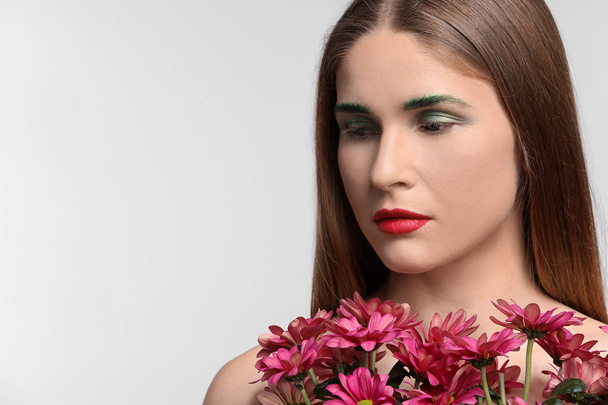 schöne Frau mit ungewöhnlichem Make-up und Blumen auf weißem Hintergrund - Foto, Bild