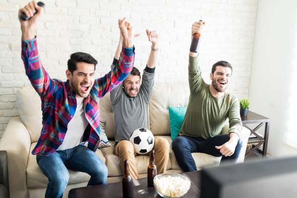Hispanic male buddies celebrating goal and screaming in front of television at home - Fotografie, Obrázek
