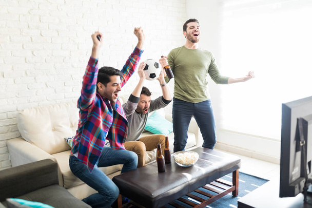 Uszczęśliwiony przyjaciółmi świętować zwycięstwo z ulubionej drużynie piłkarskiej w salonie - Zdjęcie, obraz
