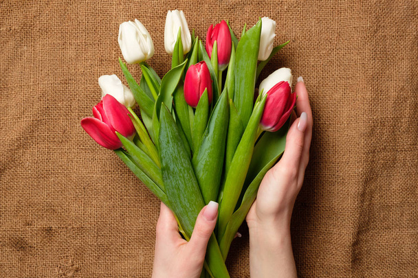 Bouquet of tulips in womans hands on rustic burlap canvas. Greeting card for International Womans Day, Mothers Day, Easter, spring holidays - Foto, immagini