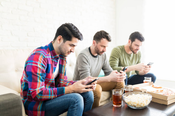 Grupo de amigos verificando suas pontuações de equipe em smartphones enquanto assiste jogo de futebol em casa
 - Foto, Imagem