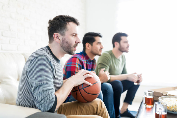 Sportovní fanoušci sledování basketbalový zápas, zatímco sedí v obývacím pokoji - Fotografie, Obrázek
