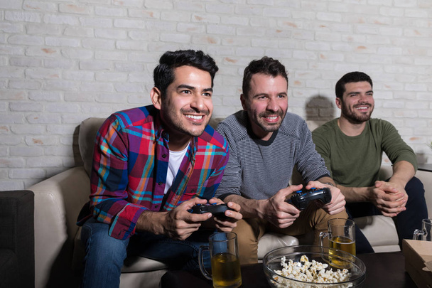 Усміхнені чоловіки грають в електронні ігри і проводять дозвілля разом вдома
 - Фото, зображення