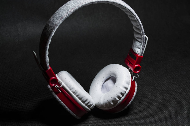 Великі портативні та різнокольорові навушники для прослуховування музики. Білий і червоний кольори. На однотонному чорному тлі
.  - Фото, зображення