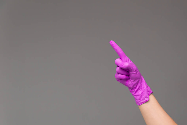 Hand in rubber glove points upwards with index finger. Neutral background , copy space. - Foto, imagen