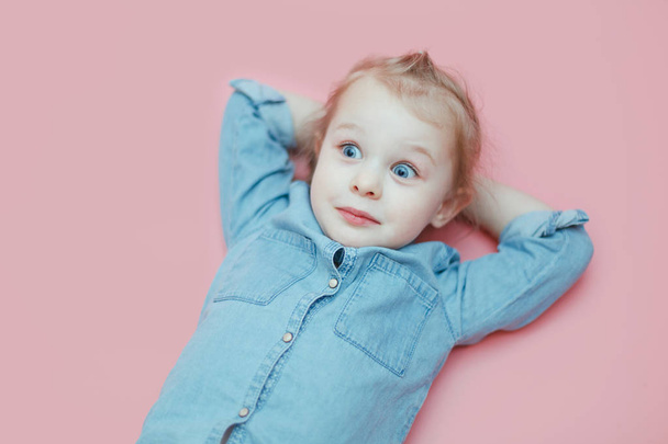 A cute white little girl is lying on a pink background with her hands behind her head. - Foto, imagen