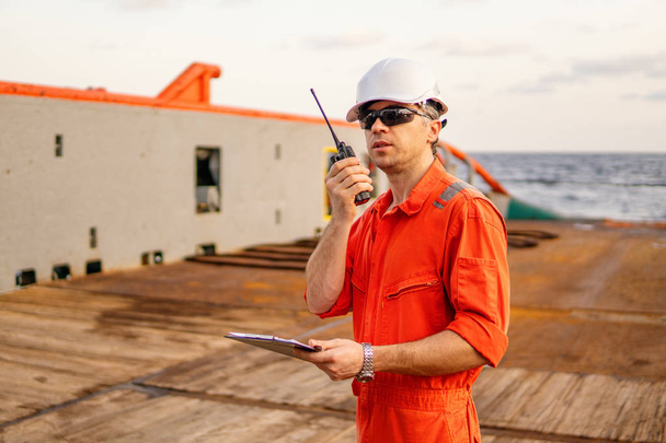 Палубный офицер на палубе оффшорного судна держит радио-рацию УКВ
 - Фото, изображение