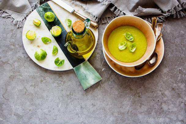 Brussels sprouts vegetable cream soup with spices in bowl and Raw Brussel sprouts over grey concrete table background flat lay. Vegan, vegetarian, healthy, dieting food concept - Image - Photo, Image
