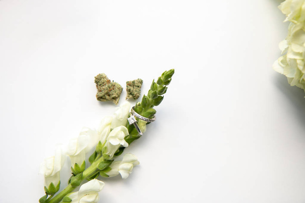 Diamantene Hochzeit und Verlobungsring auf weißer Blume mit Marihuana-Knospen von oben nach unten - Cannabis-Hochzeit - Foto, Bild