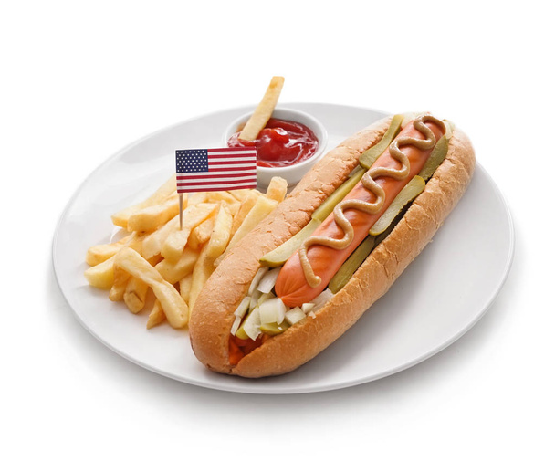 Placa con sabroso perrito caliente, papas fritas y bandera de EE.UU. sobre fondo blanco
 - Foto, imagen