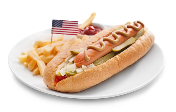 Placa con sabroso perrito caliente, papas fritas y bandera de EE.UU. sobre fondo blanco
 - Foto, imagen