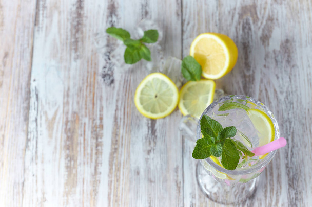 Water with lemon and mint in a glass container on a wooden table. place for text. refreshing summer citrus drink. vertical view of the summer - Photo, image