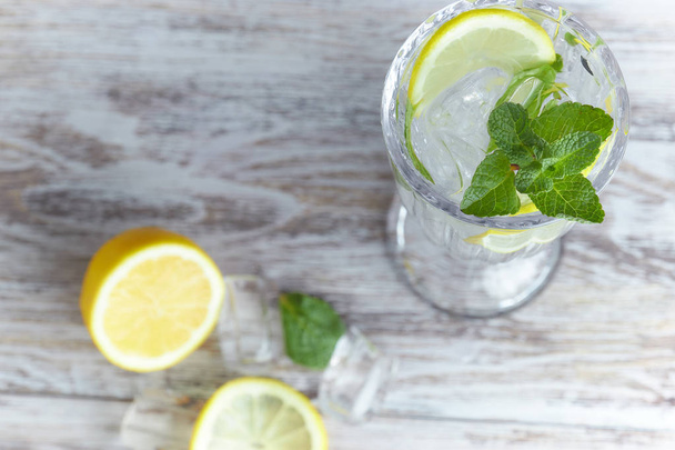 Water with lemon and mint in a glass container on a wooden table. place for text. refreshing summer citrus drink. vertical view of the summer - Photo, image