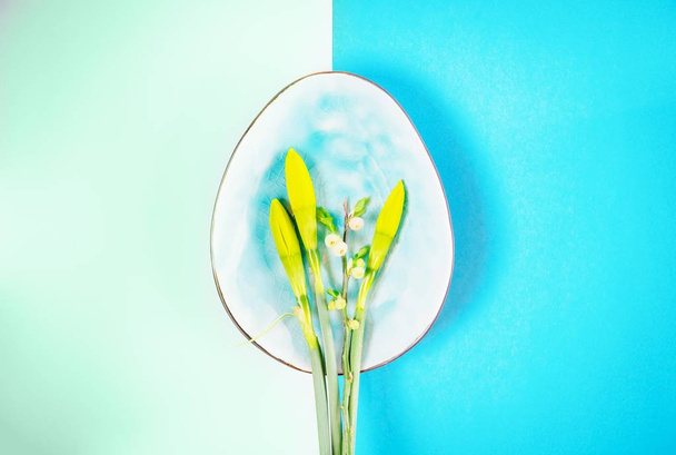Plate in shape of egg with narcissus buds and spring branch on a magic green color and blue background. Copy space - Photo, Image