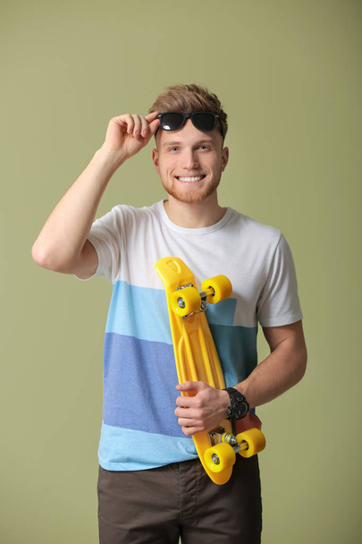 Fashionable young man with skateboard on color background - Fotoğraf, Görsel