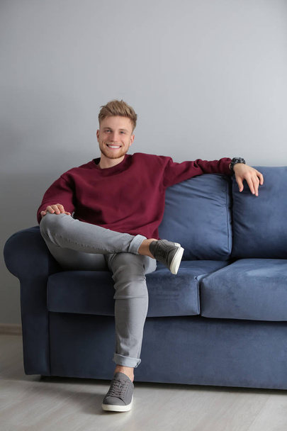 Fashionable young man sitting on sofa indoors - Foto, afbeelding