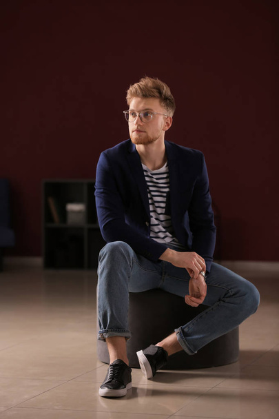 Fashionable young man sitting on pouf indoors - Photo, Image