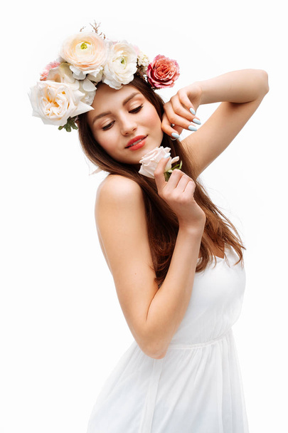 Beautiful young girl smiling and posing with flowers on white background in white dress. Studio portrait. - 写真・画像