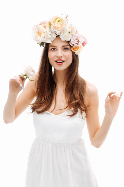 Beautiful young girl smiling and posing with flowers on white background in white dress. Studio portrait. - 写真・画像