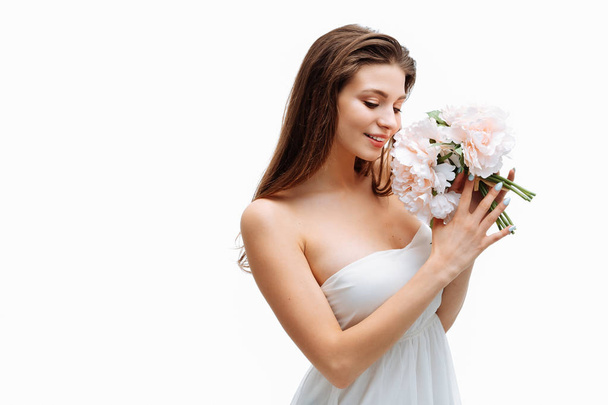 Portrait beautiful young girl smiling and posing with artificial flowers on white background in white dress. - Fotó, kép