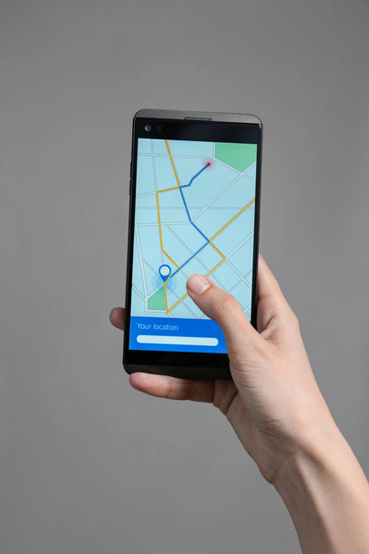 Femme tenant un téléphone mobile affichant la carte avec l'itinéraire à l'écran sur fond gris
 - Photo, image