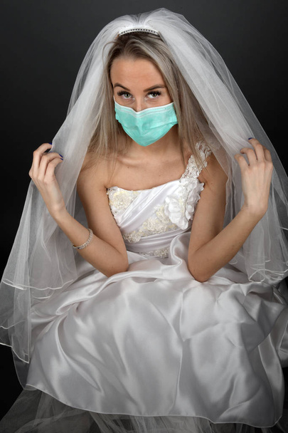 Schöne blonde Braut in einem weißen Kleid mit medizinischer Maske - Foto, Bild
