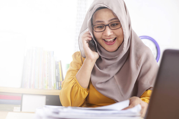 Портрет мусульманской предпринимательницы, носящей хиджаб в офисе, разговаривающей по телефону, счастливое улыбающееся выражение, имеющее хорошие новости
 - Фото, изображение