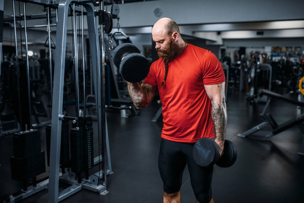 Atleta muscular haciendo ejercicio con pesas en el gimnasio. Barbudo hombre en el club deportivo, estilo de vida saludable
 - Foto, imagen