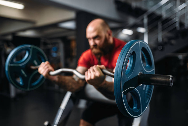 Muscular athlete doing exercise with barbell in gym. Bearded man on workout in sport club, healthy lifestyle - Foto, afbeelding