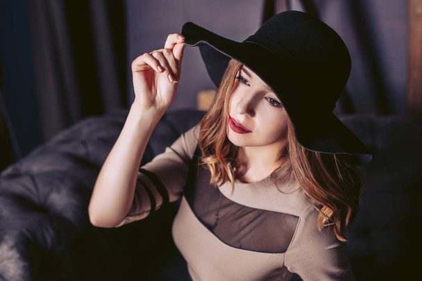 Portrait of a young girl in a classic black hat. The girl is sitting on the couch. - Foto, Imagem