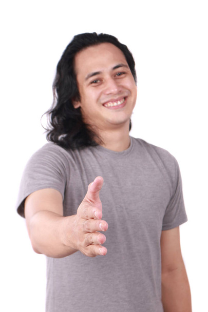 Portrait of good looking long haired young Asian man shows hand shake offer gesture with his finger isolated on white - Fotó, kép