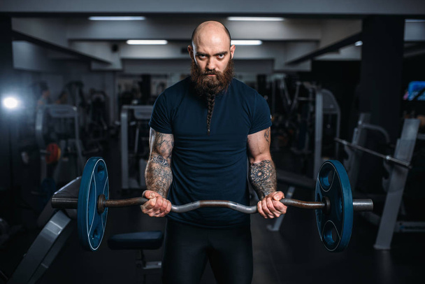 スポーツ ウエアで筋運動選手は重量、ジムでトレーニングします。スポーツ クラブでのエクササイズのひげを生やした男 - 写真・画像