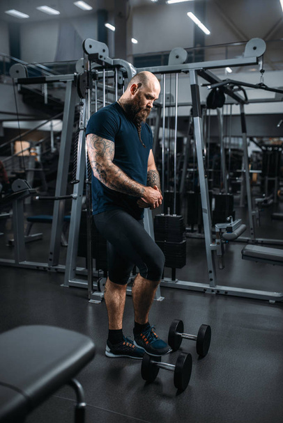 Strong athlete with dumbbells, training in gym. Bearded sportsman on workout in sport club - 写真・画像